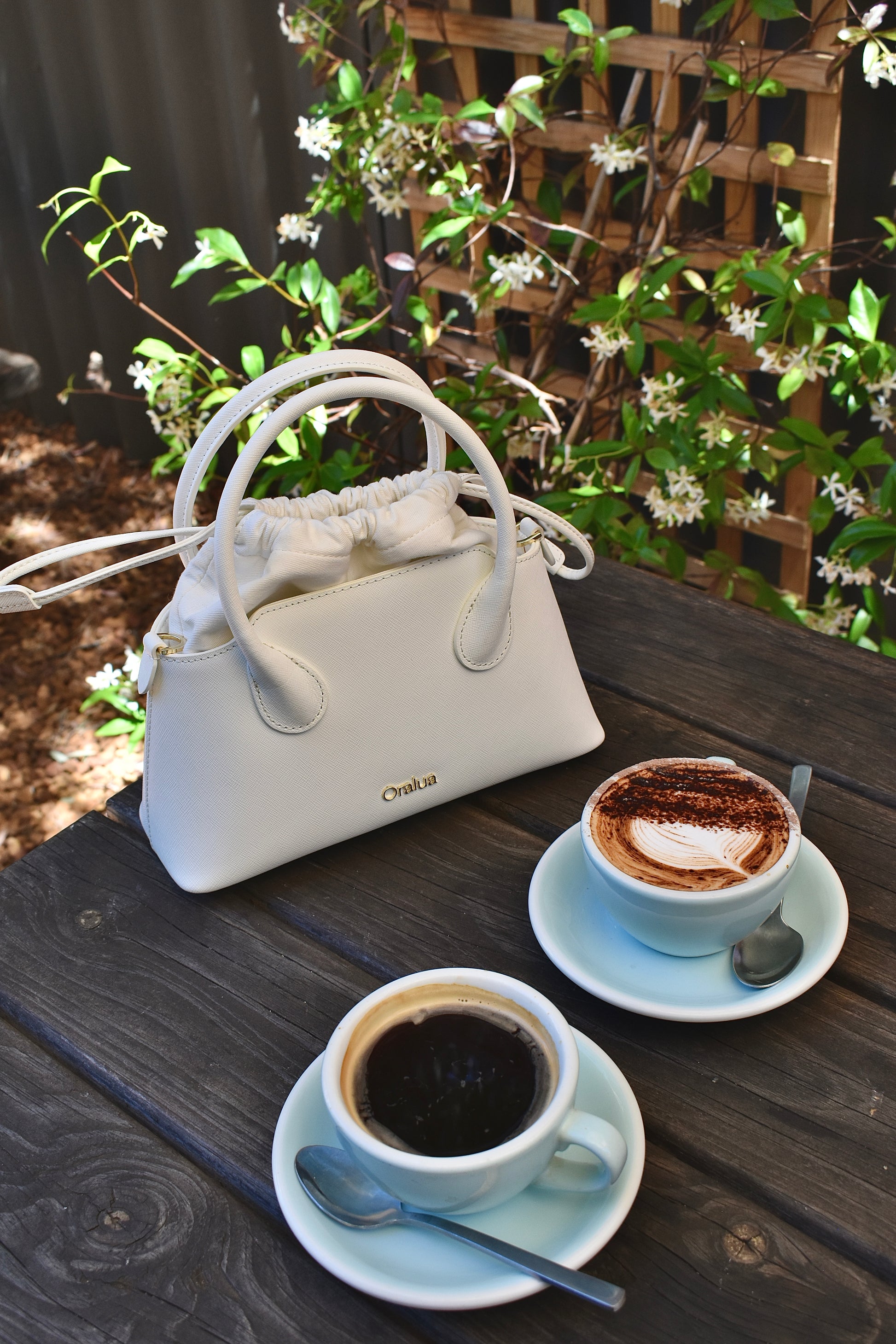 White handbag on a wooden table with two cups of coffee and saucers.