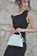 Woman holding a white handbag against a stone wall