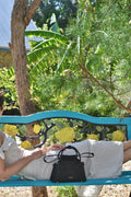 Person sitting on a blue bench with a black handbag in a garden setting