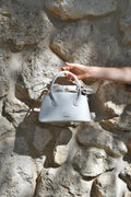 White handbag being held against a stone wall