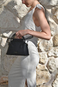 Person holding a black handbag against a stone wall